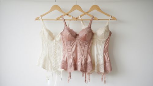 Structured Lingerie Styles Hanging corset, bustier, and basque on white wall. Ivory and rose tones.