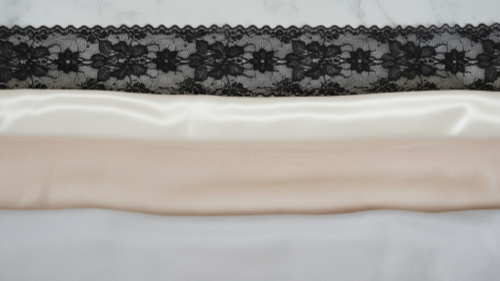 Fabric samples of lace, satin, mesh, and cotton on white marble.
