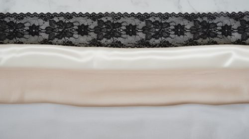 Lingerie Fabric Textures Fabric samples of lace, satin, mesh, and cotton on white marble.